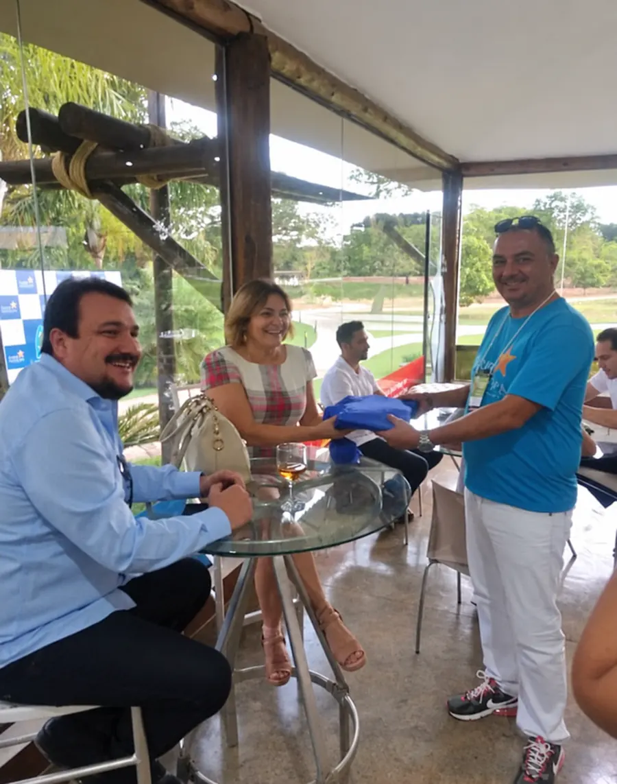 Benedito entregando um presente a uma cliente sentada à mesa