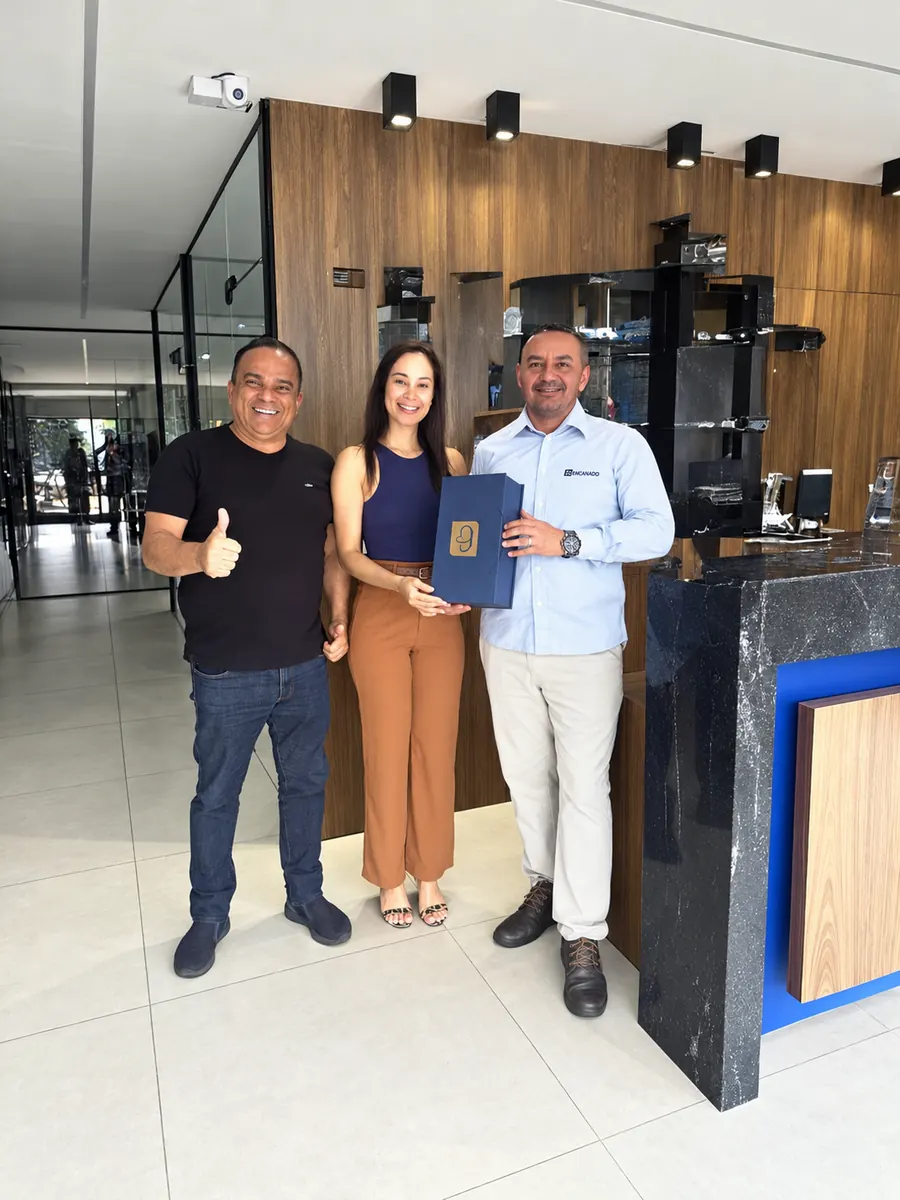 Benedito com dois clientes em uma loja, um deles segurando uma caixa de presente