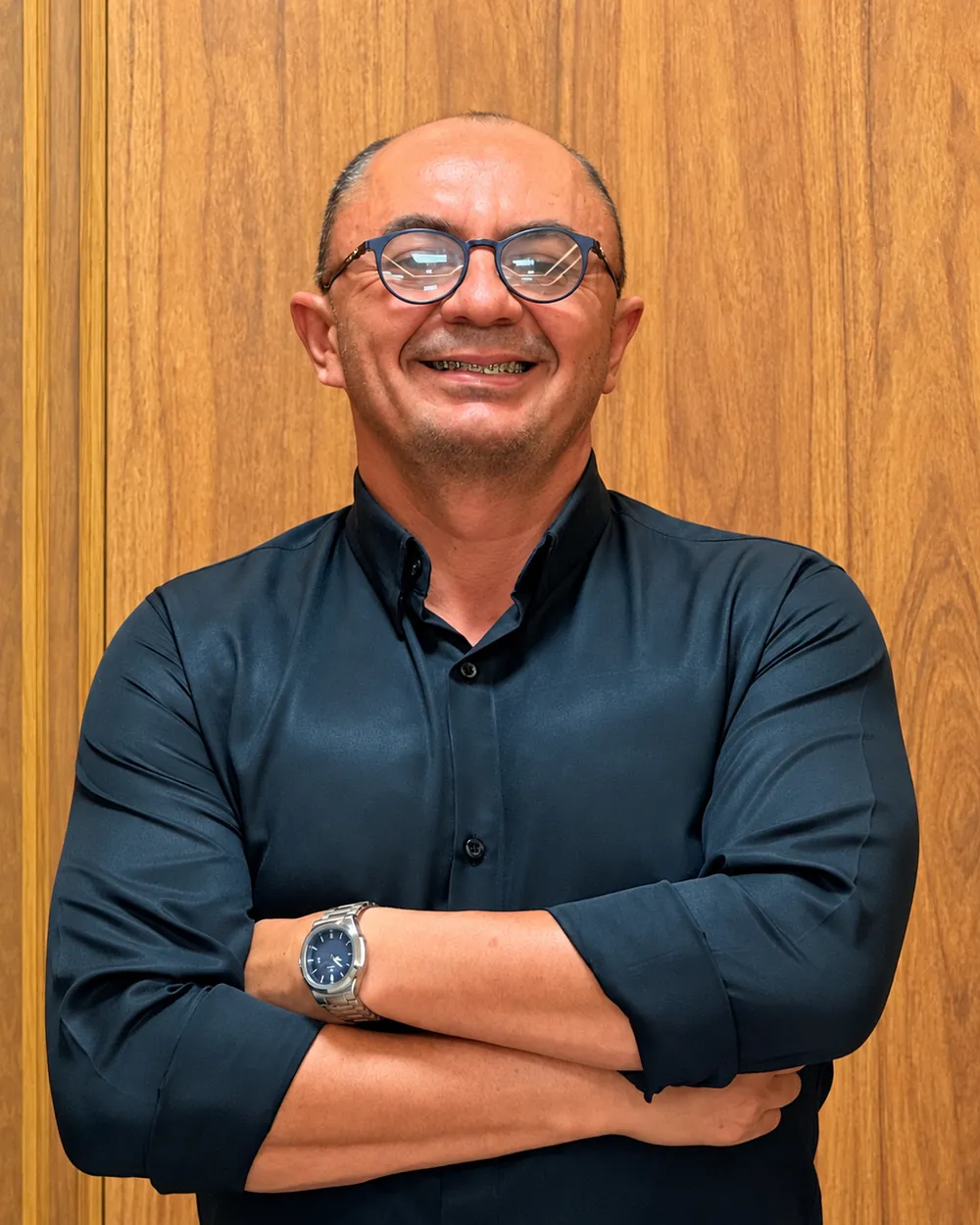 Benedito Bezerra Madeiro, corretor de imóveis, de braços cruzados diante de um painel de madeira